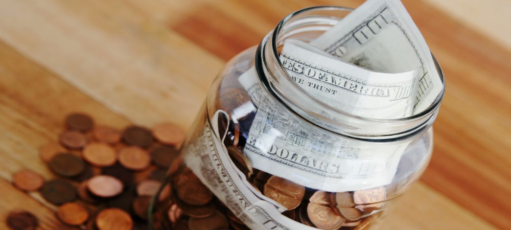 Coins on wooden table next to a mason jar with bills