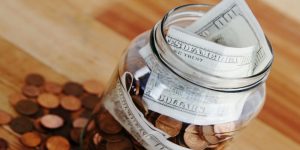 Coins on wooden table next to a mason jar with bills